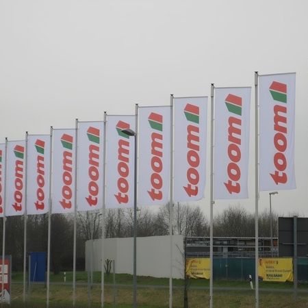 Eine Mastenreihe mit Toom Flaggen vor einem Toom Baumarkt