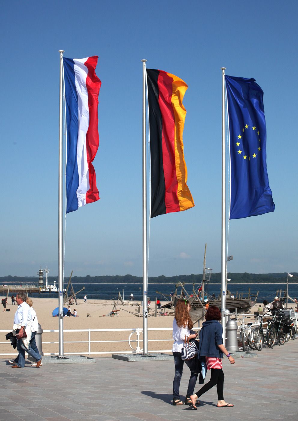 Eine deutsche, niederländische und europäische Fahne wehen an einem Fahnenmast am Strand im Wind