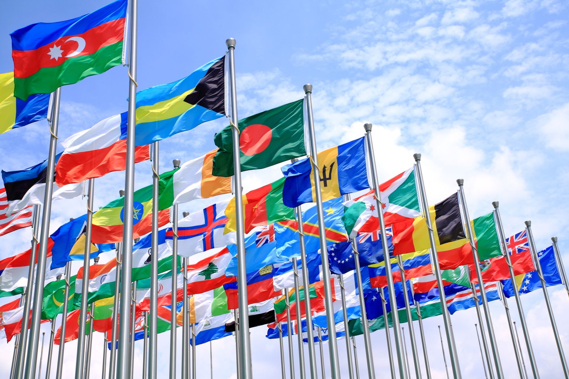 Mehrere Landesflaggen wehen an Fahnenmästen im Wind vor blauem Himmel im Hintergrund