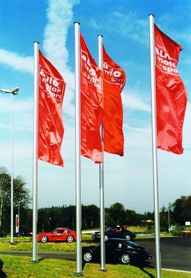 Mehrere rote AUTO MOTOR UND SPORT Fahnen wehen im Wind auf einem Parkplatz mit Autos im Hintergrund