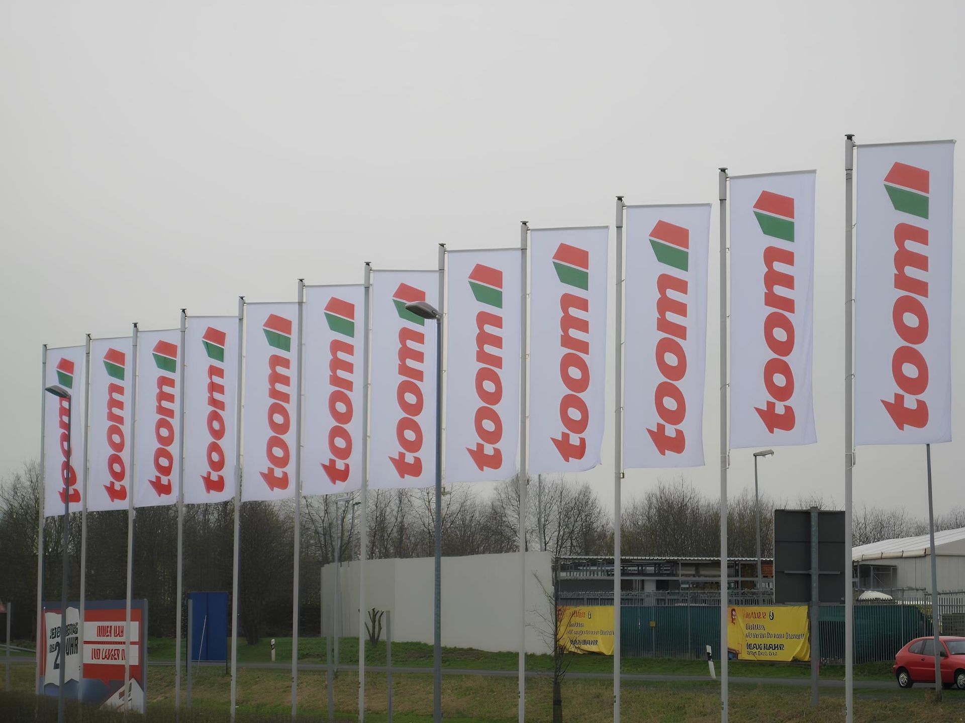 Typ 2 Mastenreihe vor einer Toom Baumarkt Filiale mit Fahnen mit dem Toom Logo